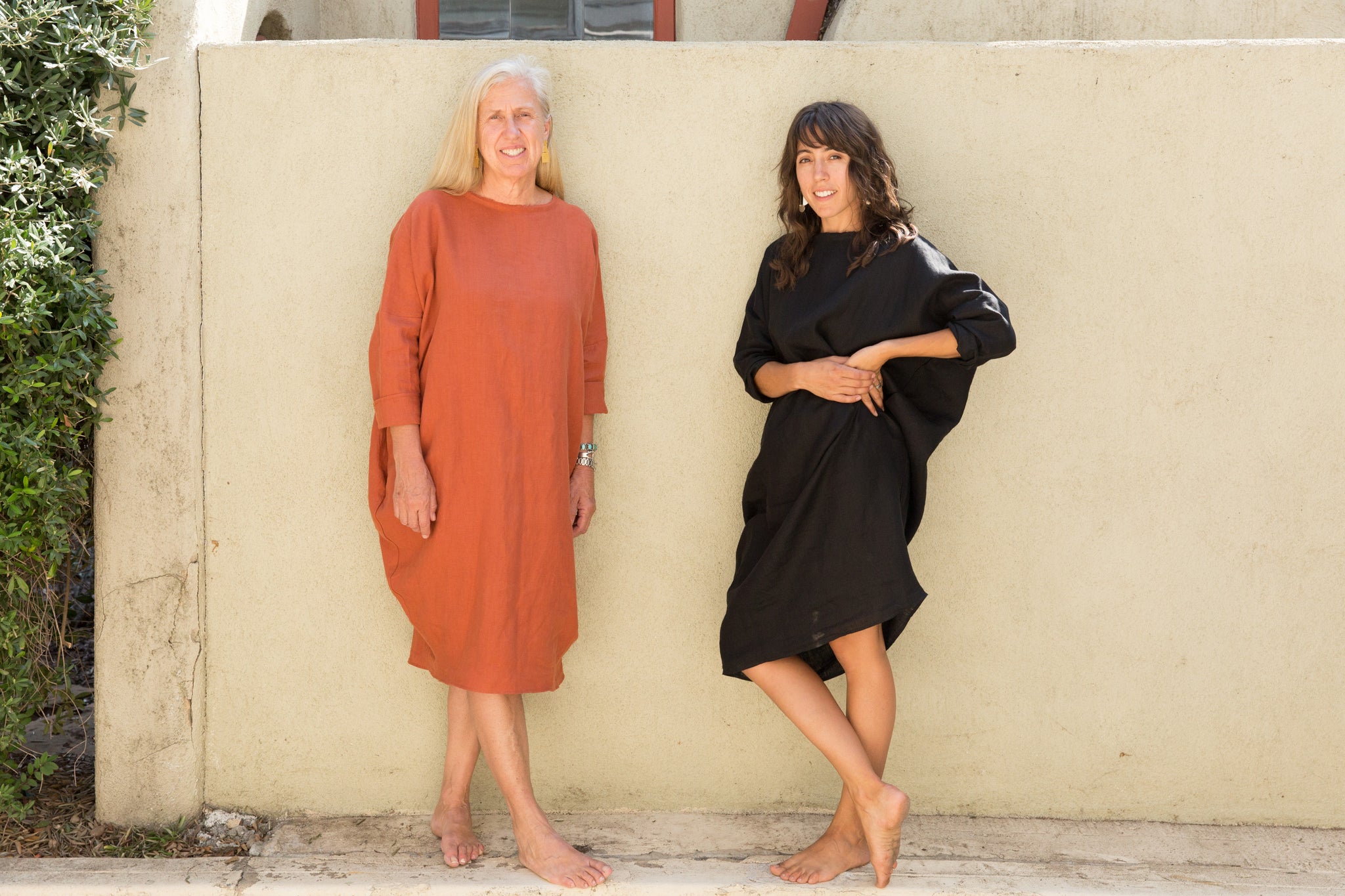 Dotter owners, Susanne McLean and Annika Huston, wearing Robyn King dresses in front of green wall