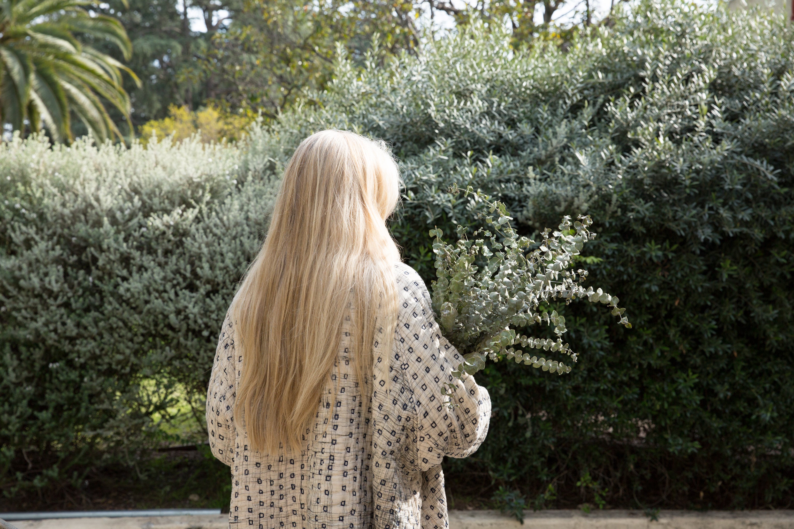 back view of Susanne McLean wearing Pavo jacket, holding a bouquet of eucalyptus