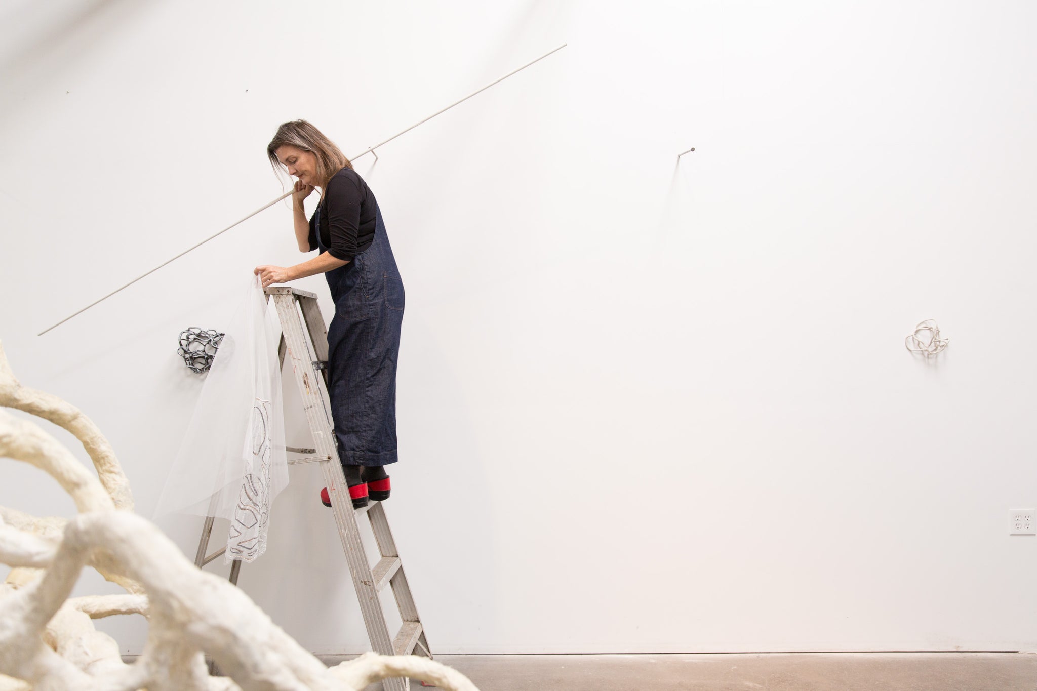artist, Laura Cooper, on ladder installing artwork