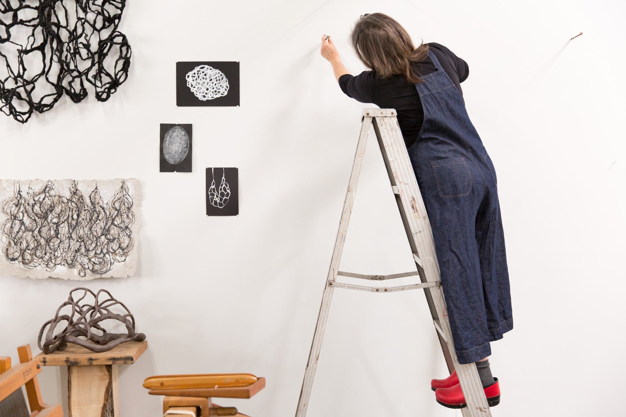 artist, Laura Cooper, on ladder installing artwork