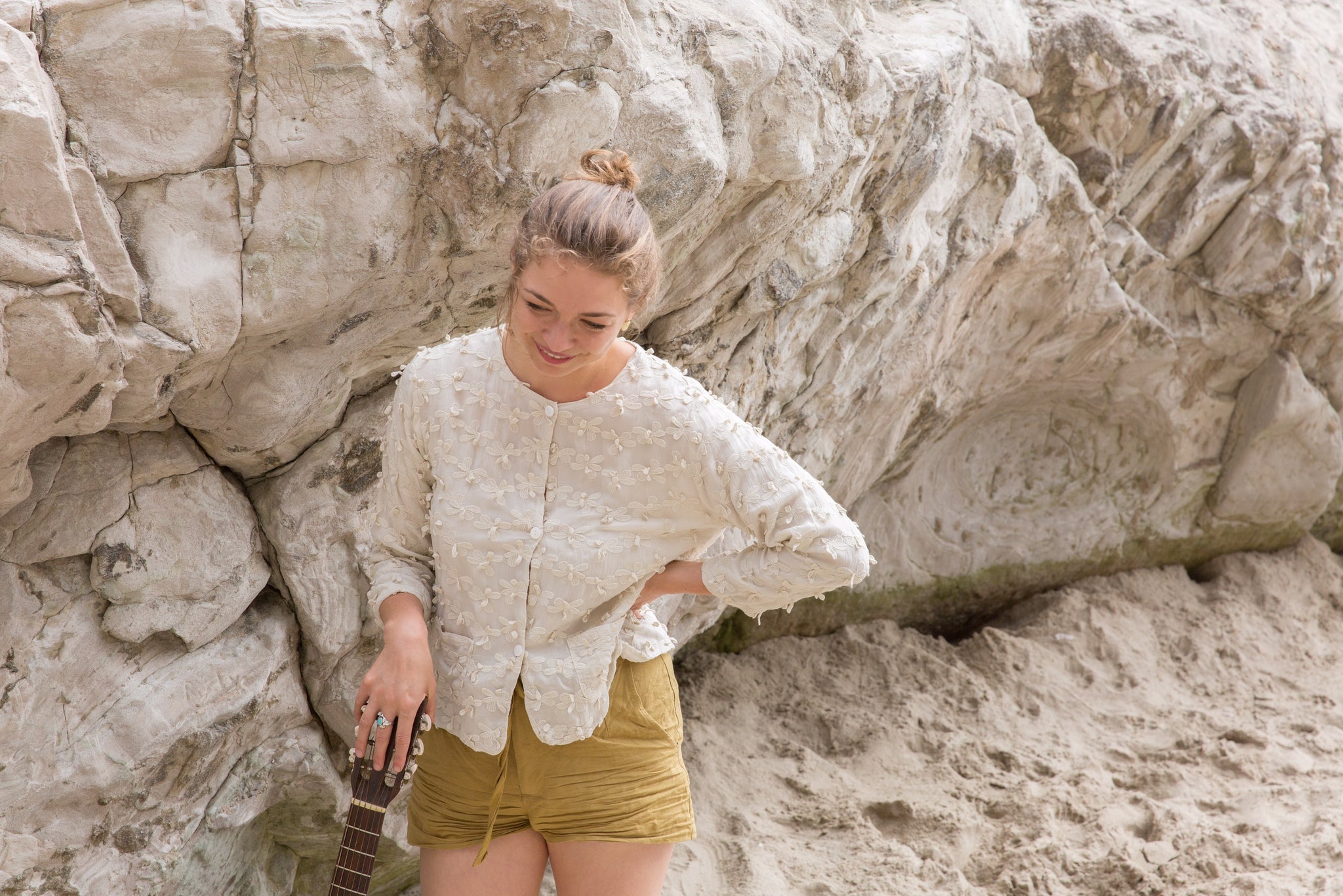 Portland musician, Hanna Haas, resting against guitar on beach and wearing CP Shades jacket