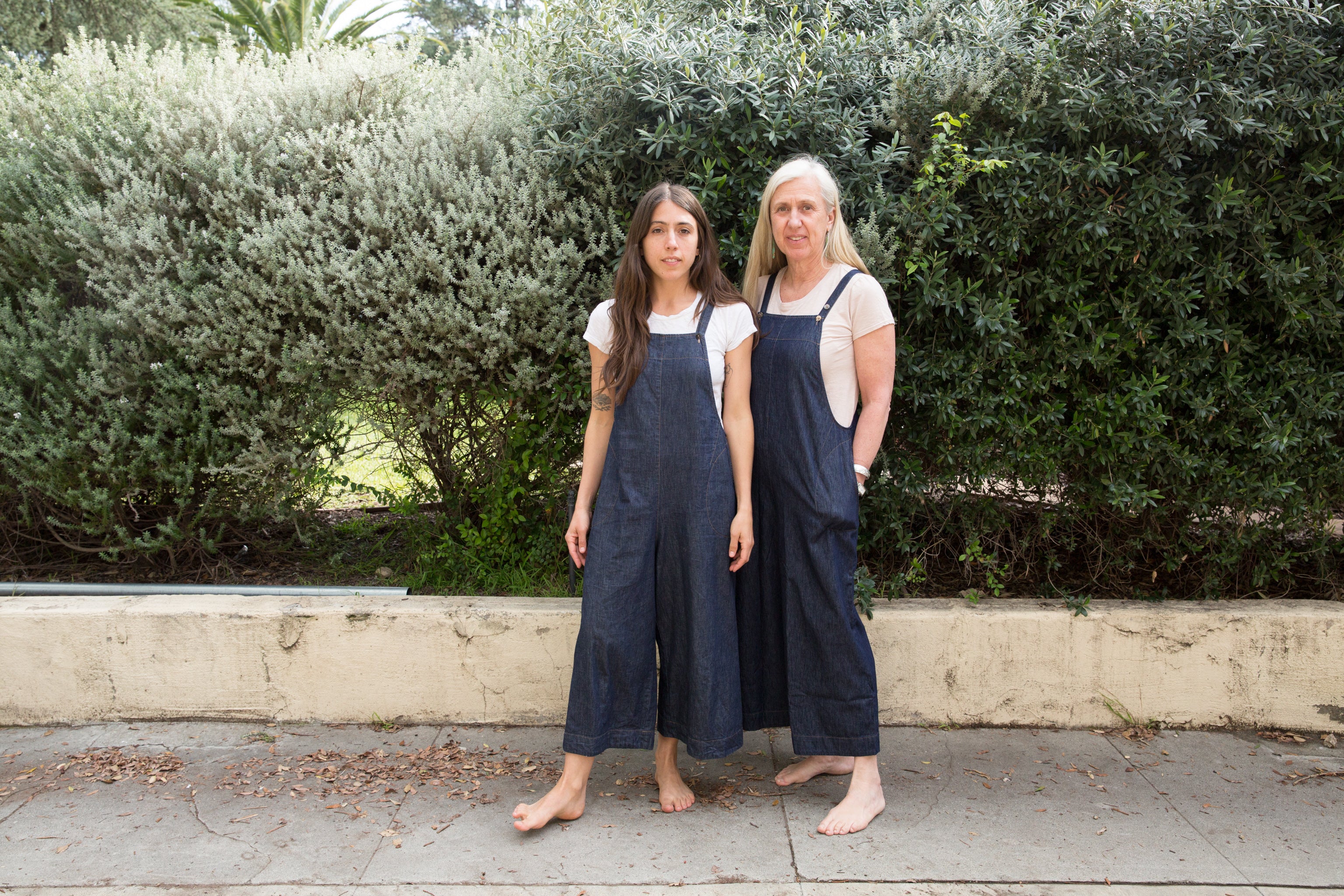 Dotter owners, Annika Huston and Susanne McLean, wearing denim jumpsuits in front of bushes