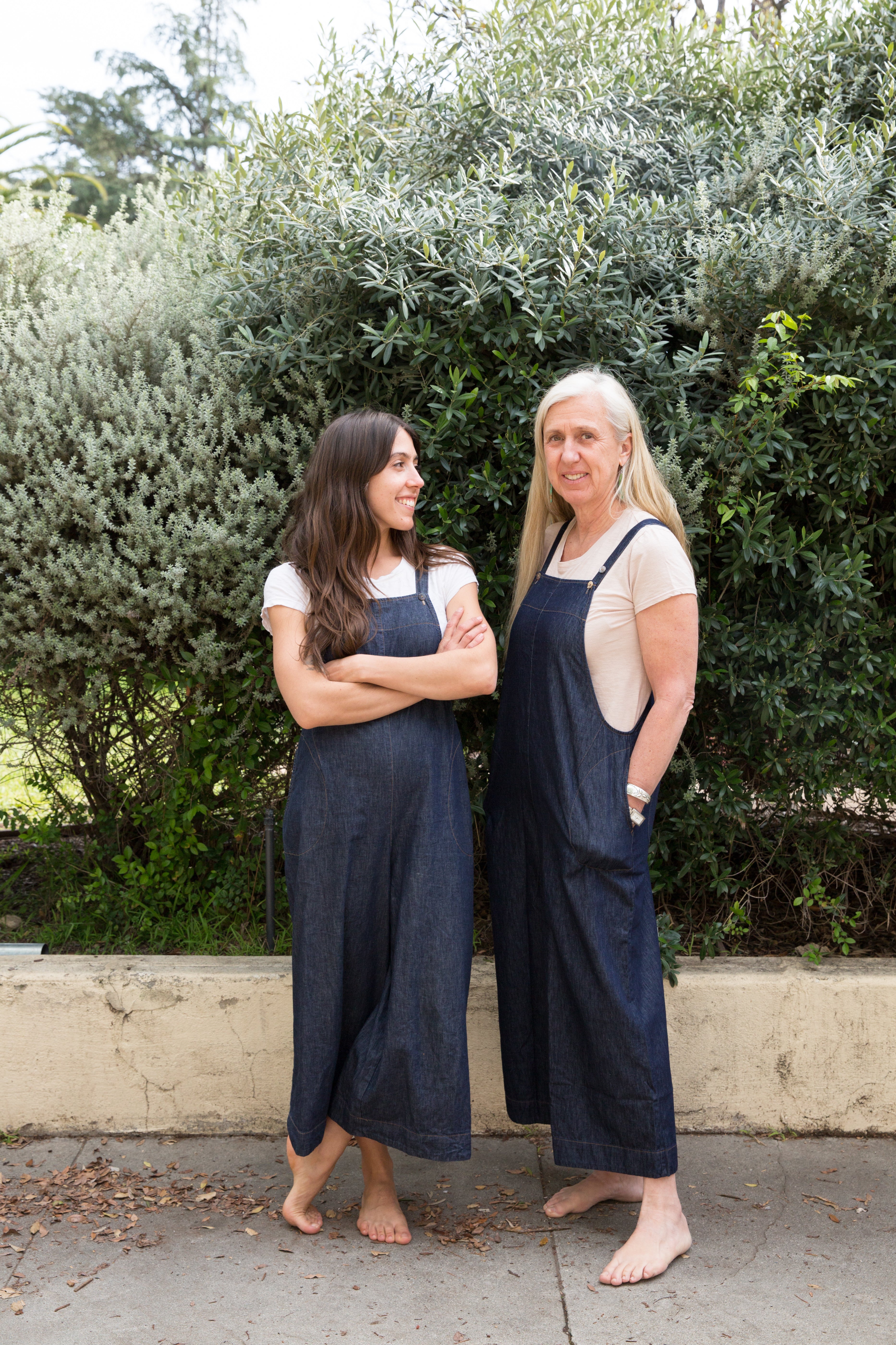 Dotter owners, Annika Huston and Susanne McLean, wearing denim jumpsuits in front of bushes