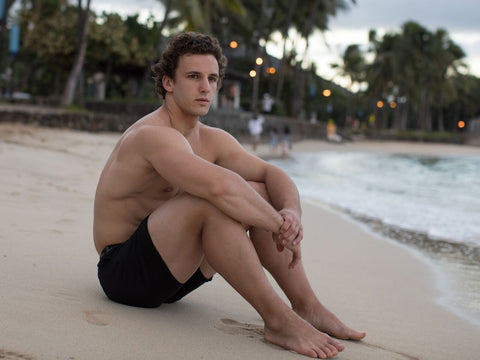 male model sitting on beach in black men's boxers