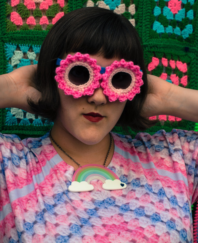 Ashley Zhong models a pair of crocheted sunglasses or funny sunnies in front of a wall of granny squares