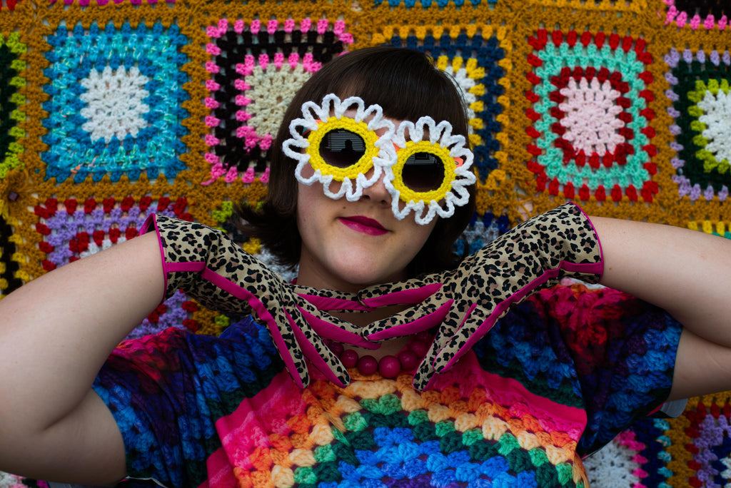 Ashley Zhong modeling crocheted sunglasses in front of a wall of granny squares