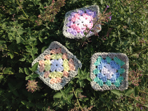 gray and pastel granny squares on a bed of purple flowers