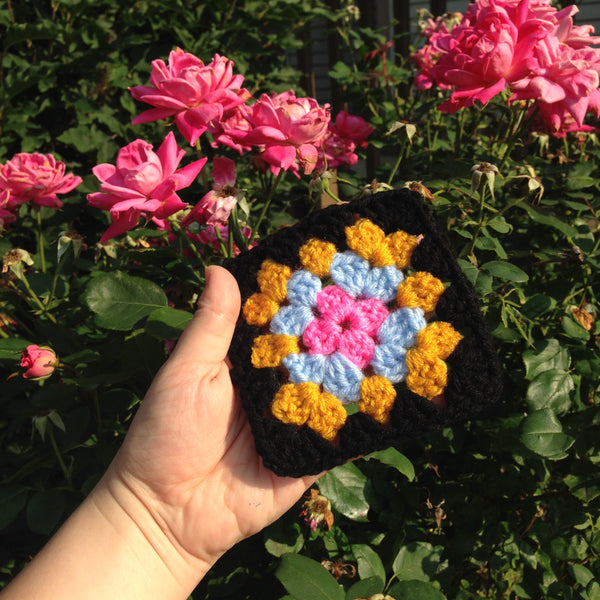 A classic granny square with a black border in front of a rose bush
