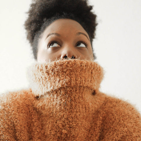 Black woman with afro puff looking up pulling her jumper over her face