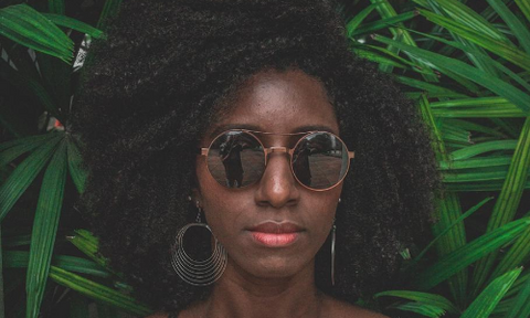 black woman in front of palm leaves with sunglasses on 
