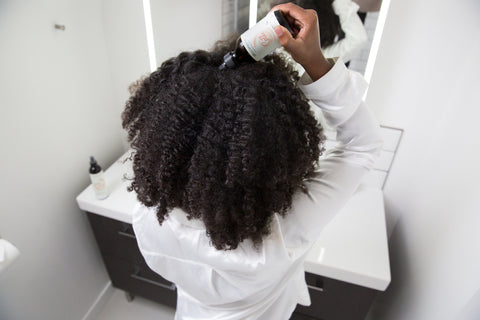 Itchy scalp: back view of black woman applying oil to scalp