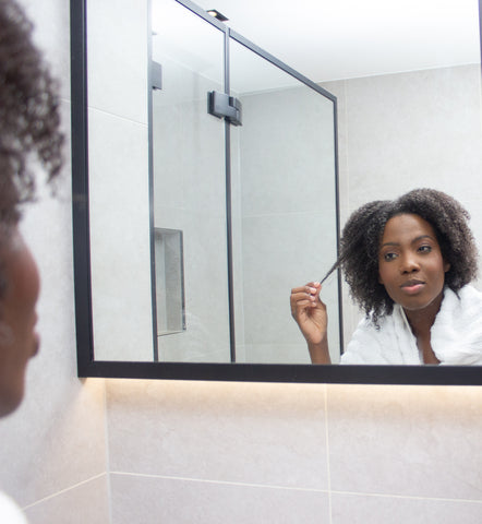 Itchy scalp: Young black woman looking in the mirror touching hair