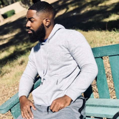 Black man with beard wearing grey and sitting on a bench