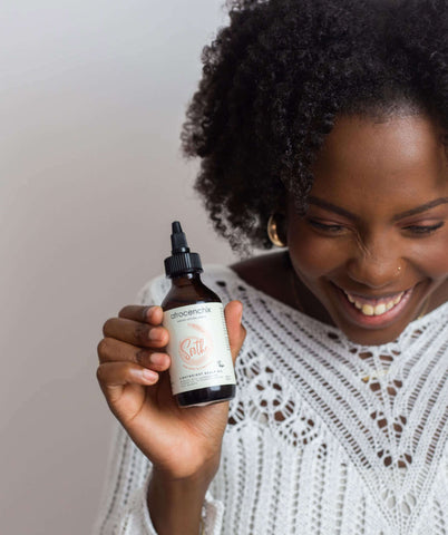 Itchy scalp: Smiling black woman holding Afrocenchix Soothe Oil