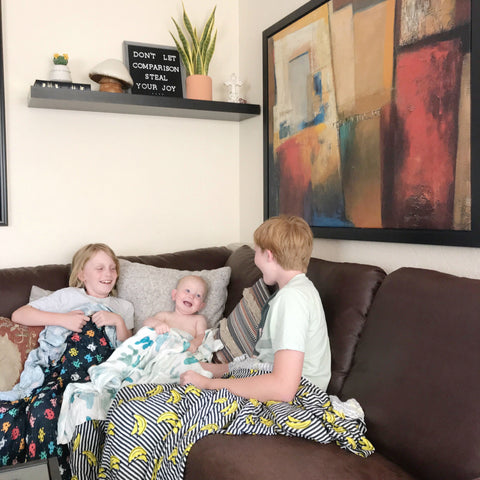 Three siblings laughing at each other while sitting on a sofa.