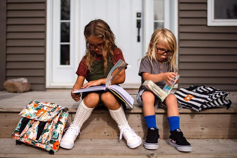 Two siblings reading and sitting on their front porch.