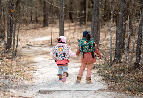 Two children, visible from the back, walking through the woods.