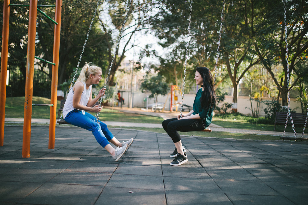 Zwei Frauen sitzen sich auf einer Schaukel gegenüber und lachen. Mit Conversational Commerce kannst du deiner Kundschaft stets zur Seite stehen.