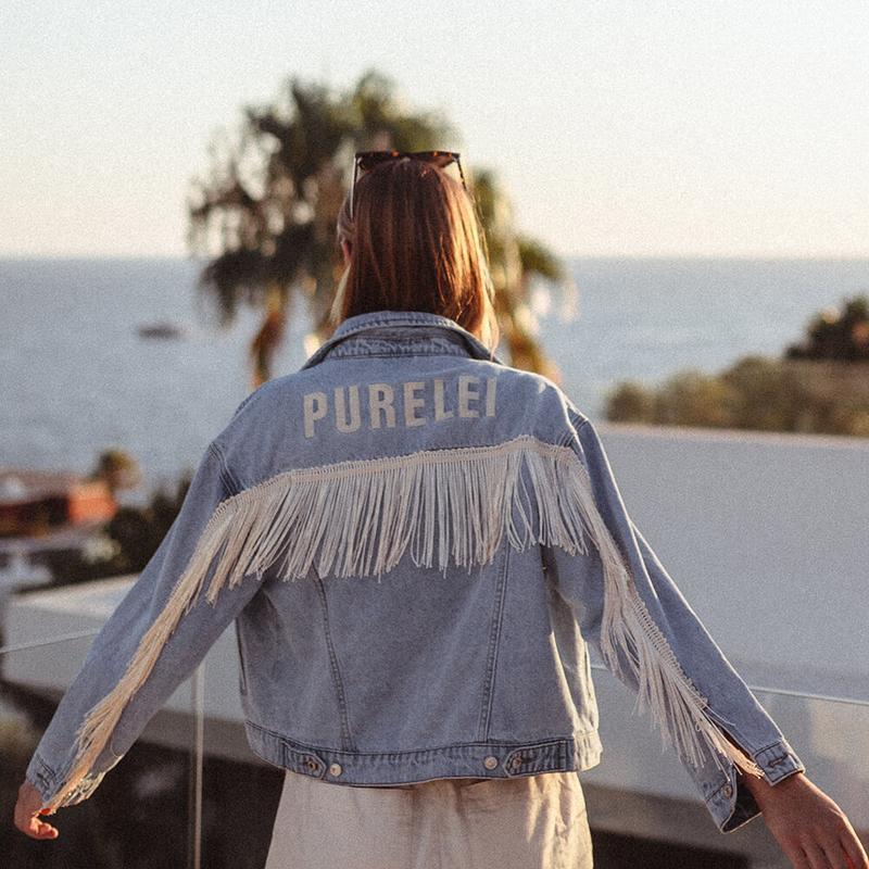 Eine Frau, die am Strand eine Jacke mit der Aufschrift PURELEI trägt. 