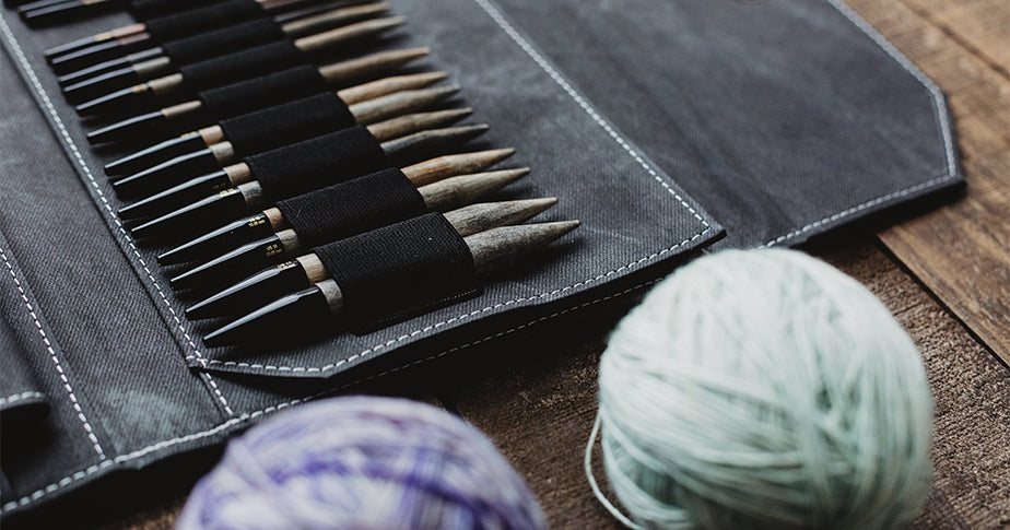 Nahaufnahme einer Stricknadelsammlung und einem Garnball auf einem Holztisch. Mit Hobby Geld verdienen: Wir zeigen dir, welche Wege es gibt!