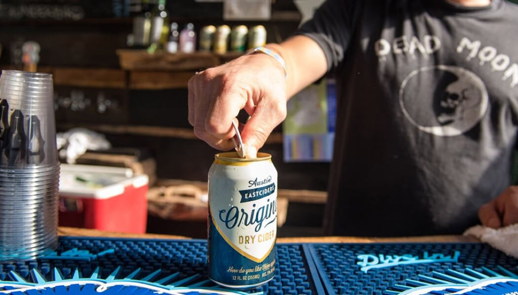 Man behind a bar opening a chilled can of Austin Eastciders Original Dry hard cider