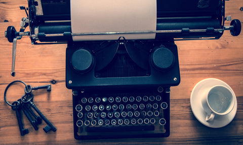 Keys, a typewriter, and a teacup and saucer sit on a wooden table.