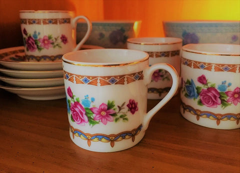 A set of four teacups and saucers with flowers on them are arranged on a table.