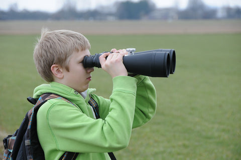 young boy looking through binoculars outside
