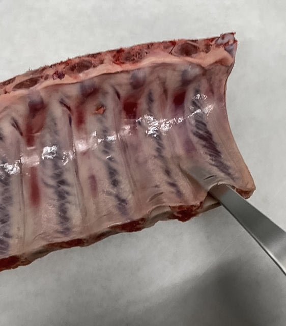Photo showing a knife removing the membrane from the back on a rack of ribs