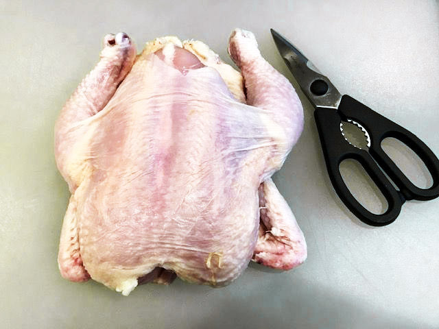 Photo of raw whole chicken next to a pair of kitchen shears