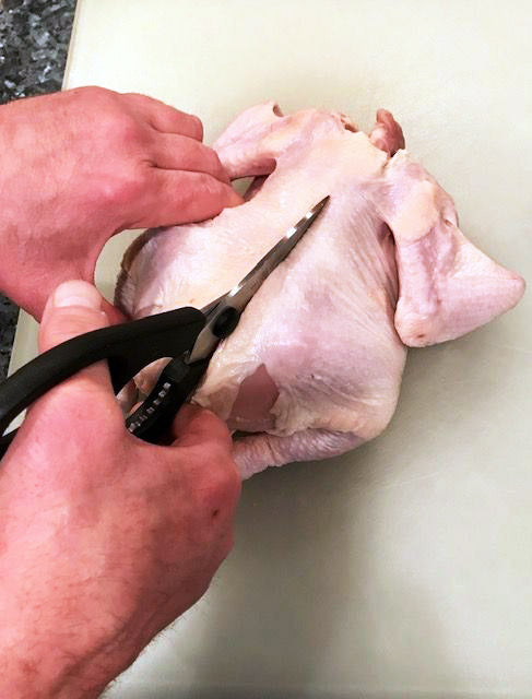 Photo of whole raw chicken with kitchen shears cutting along backbone
