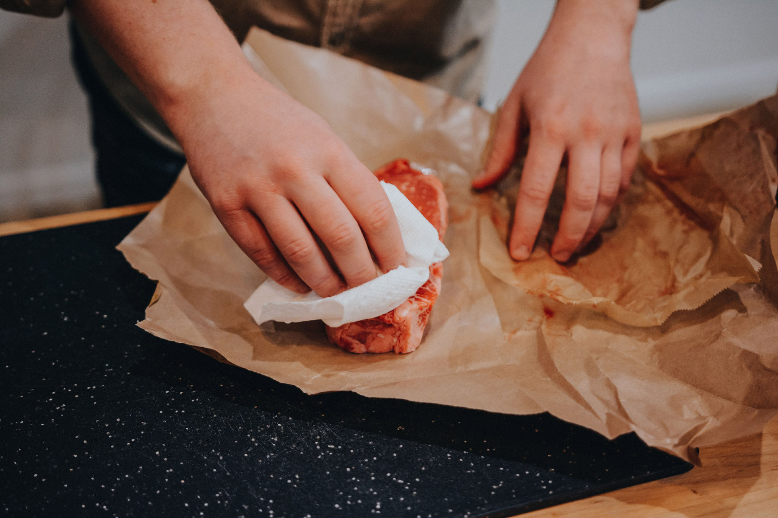 Hand using paper towel to dry raw steak