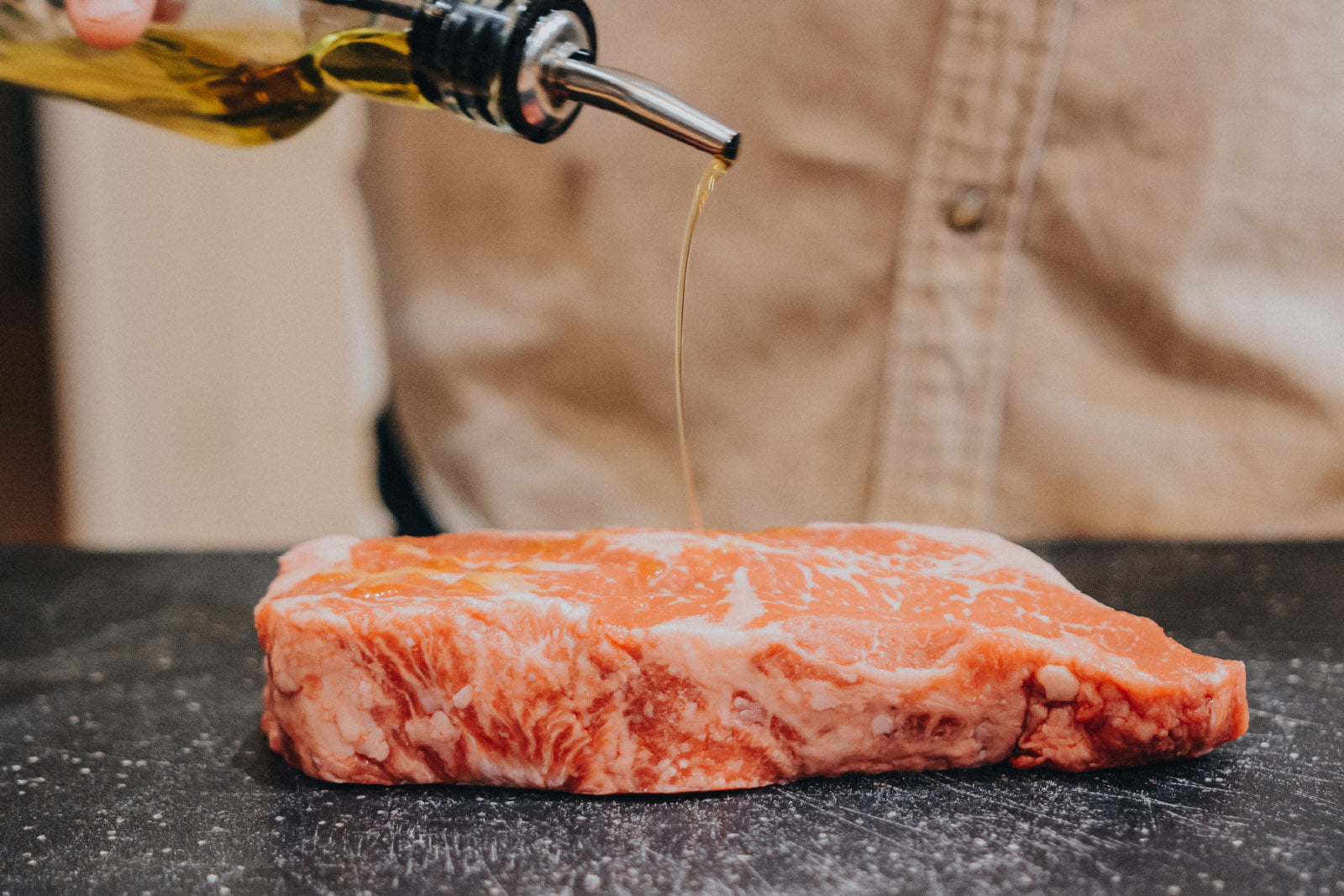 Raw steak with olive oil being poured on it