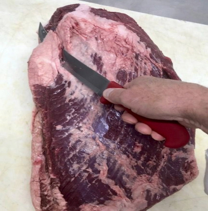 Photo of raw beef brisket being trimmed with a large knife