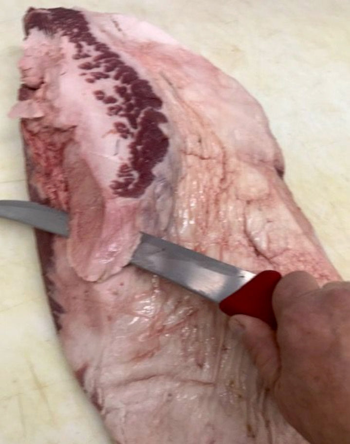 Photo of raw beef brisket being trimmed with a large knife