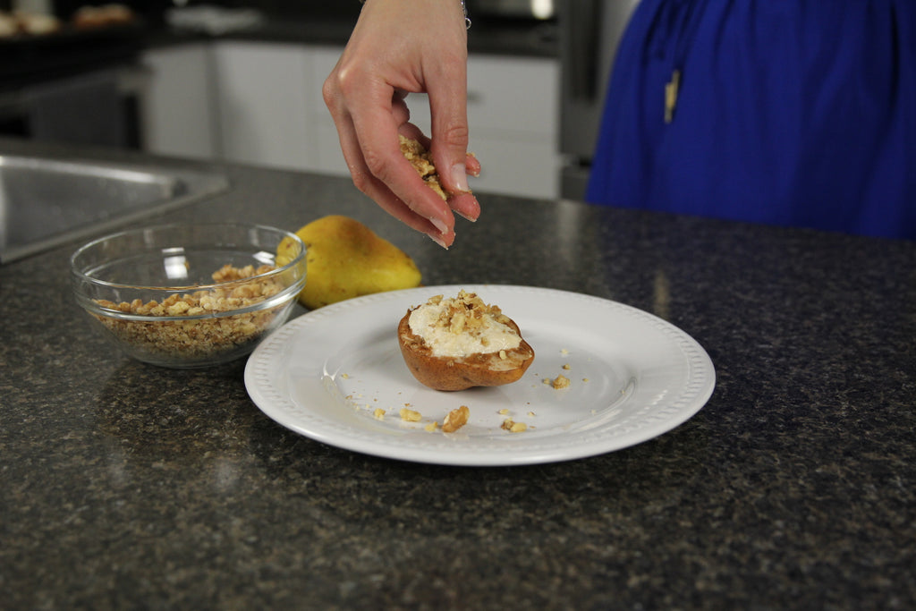 woman pouring walnuts on a baked pear 