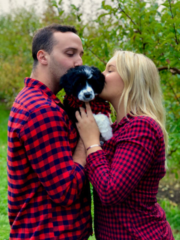 Are You Ready For a Puppy? | small black and white PWD puppy is being held in between two owners. They are all dressed in buffalo plaid and the owners are kissing her head. | Bubu Brands 