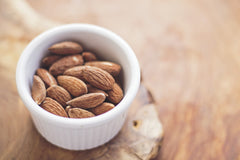A bowl of almonds in a light colored bowl on a wood table | Bubu Brands