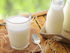 A glass of light colored milk with a spoon next to it and a glass jar of light colored milk | Bubu Brands