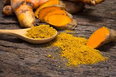 A spoon of bight tumeric powder and pieces of tumeric sliced in half | Bubu Brands