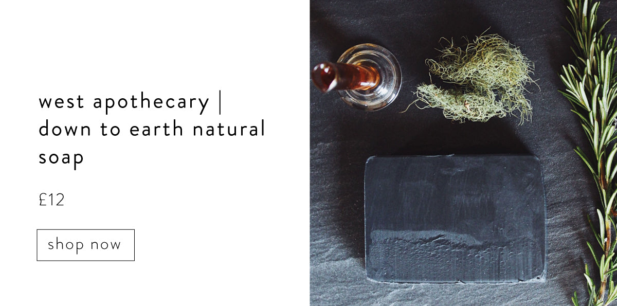 West Apothecary down to Earth natural soap. Black bar of soap on slate background next to a sprig of Rosemary.