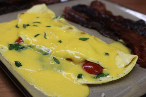 A delicious Florentine omelet with red tomatoes and several slices of maple bacon