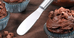 A RADA Party Spreader with a black resin handle propped up against a chocolate cupcake with chocolate frosting and shavings