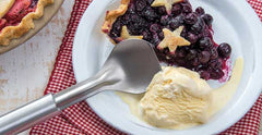A RADA Ice Cream Scoop with a silver brushed aluminum handle next to a slice of blueberry pie with a star shaped crust and a scoop of vanilla ice cream