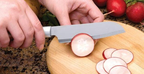 A Rada Cook's Utility knife slicing a red radish over a circular wooden cutting board with several slices already cut