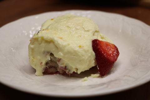 An orange and strawberry sweet roll with white creamy frosting on top next to a strawberry on a white plate
