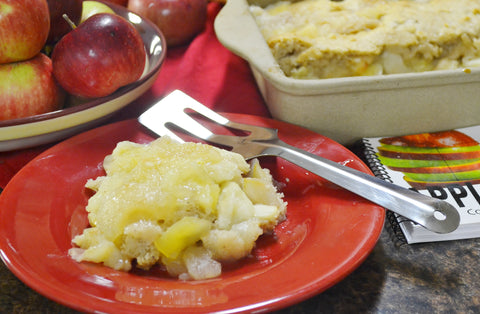 A RADA stainless steel Serverspoon next to a slice of apple cobbler and a bowl of apples and another pan of apple cobbler
