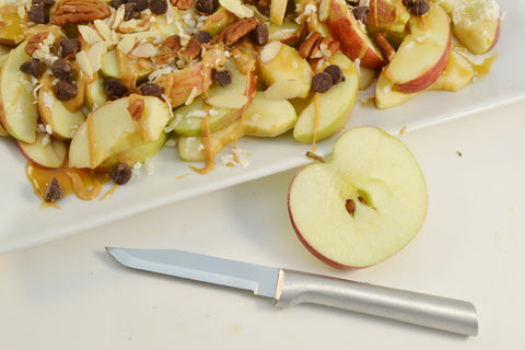 A RADA high carbon stainless steel Regular Paring Knife with a silver brushed aluminum handle next to a halved apple and some apple-crisp on a white platter