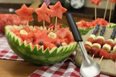 Finished watermelon bowl decorated with slices of bananas, blueberries, cubes of watermelon and star skewers next to some fruit kabobs and a RADA Ice Cream Scoop leaning up against it