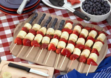 American flag themed strawberry, banana, and blueberry fruit kabobs on a ceramic board